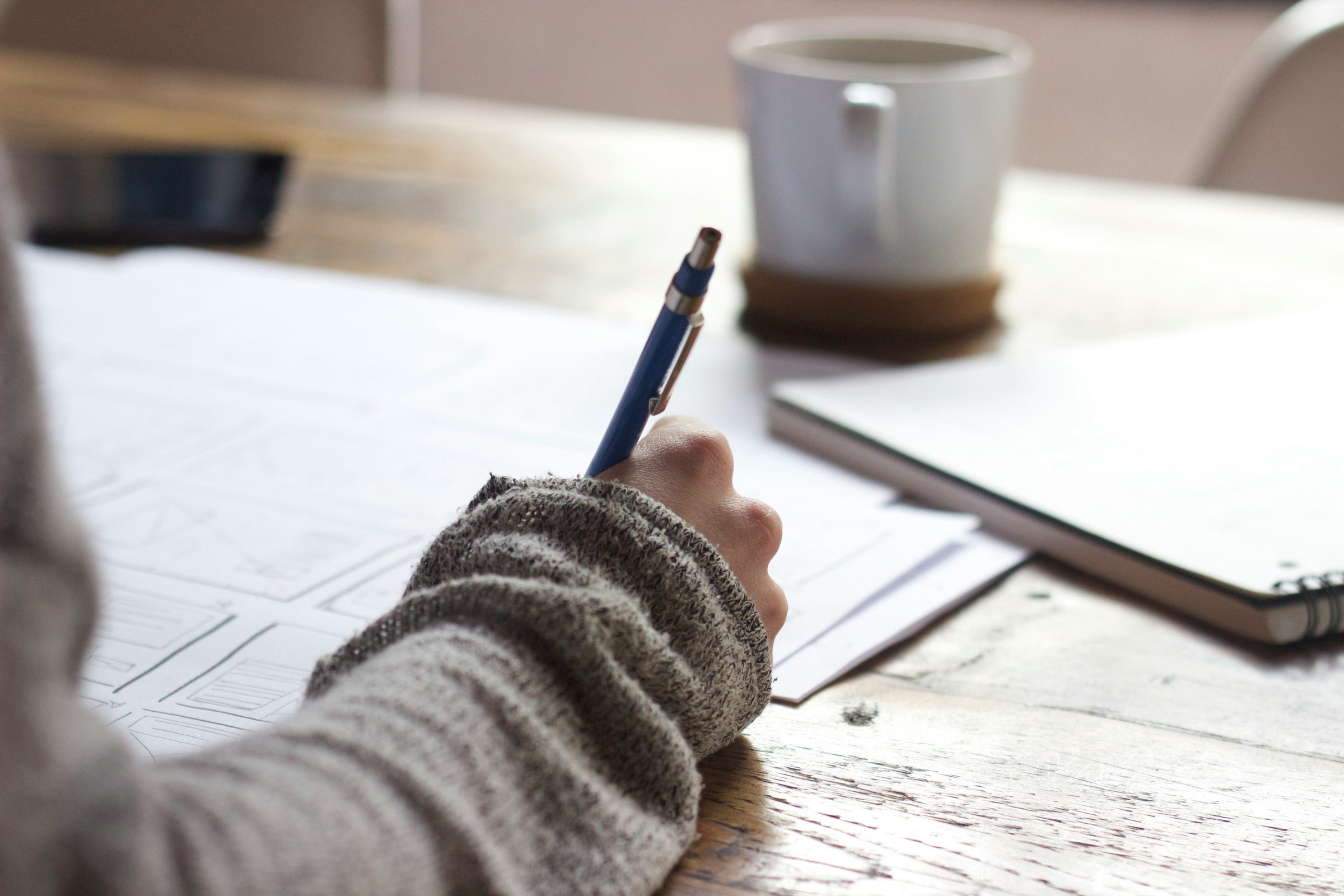 Notes being written by hand beside a coffee